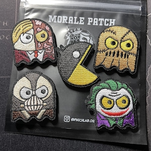 May include: Five embroidered morale patches featuring various characters in a ghost-like shape. The patches are on a black background with the text "MORALE PATCH" and "@PATCHLAB.DE" visible. The characters include a Pac-Man, a Joker, a character with a mask, a character with two faces, and a character with stitches.