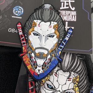 May include: A colorful embroidered patch featuring a cyberpunk samurai with a white face, black hair, and a beard. The patch has a blue, red, and yellow design with the text "Cyberpunk Samurai" in white.