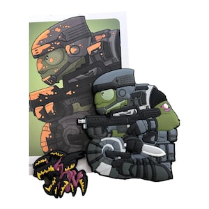 May include: A set of cartoon-style PVC charms featuring a green reptile soldier in tactical gear, holding a rifle and knife. A second charm depicts a black and yellow insect-like creature. The background shows a similar soldier.