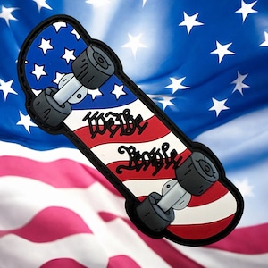 Puede incluir: Un parche de monopatín con un diseño patriótico. La parte superior presenta una sección azul con estrellas blancas, y la inferior tiene rayas rojas y blancas. Las palabras "We the People" están escritas en el centro.