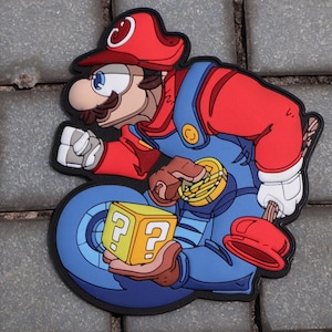 May include: A colorful, cartoon-style image of a character in a red hat and blue overalls, holding a gold coin and a yellow question mark block. The character is set against a blue wheel.
