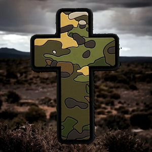 Peut inclure: Un écusson en forme de croix avec un motif camouflage. La croix présente un motif de formes vertes, marron et beige. L'arrière-plan est une scène extérieure floue avec un ciel nuageux.