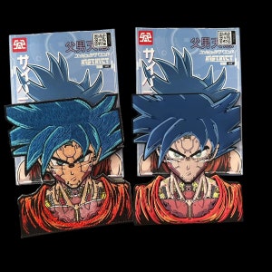 Puede incluir: Dos parches con un personaje de anime de pelo azul con detalles robóticos. El personaje viste un atuendo naranja y rojo. Los parches están sobre un fondo azul y blanco con texto japonés.
