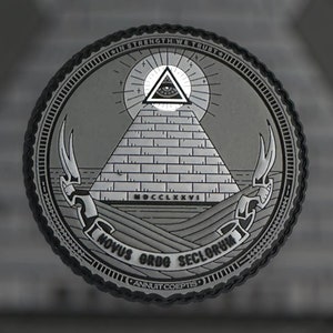 Può includere: Un emblema circolare grigio con una piramide e un occhio in cima, circondato da testo. Le parole "IN STRENGTH WE TRUST", "NOVUS ORDO SECLORUM" e "ANNUIT COEPTIS" sono visibili. È presente anche il numero romano "MDCCLXXVI".