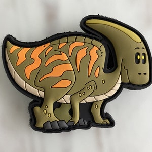 May include: A green and orange cartoon dinosaur with a large head and a long, curved horn. The dinosaur has a friendly expression and is standing on four legs.