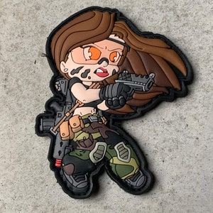 Könnte beinhalten: Eine Comicfigur mit braunen Haaren, die eine Tarnhose und ein schwarzes Oberteil trägt und eine Pistole und ein Gewehr hält. Die Figur hat orange Augen und schwarze Gesichtsbemalung.