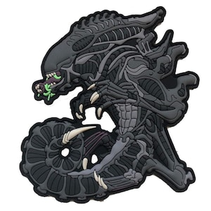 Pode incluir: Um patch cinza e preto com uma representação detalhada de um Alien Xenomorph. O design inclui a cabeça da criatura, dentes afiados e estrutura esquelética. O patch tem um efeito 3D e está sobre um fundo branco.