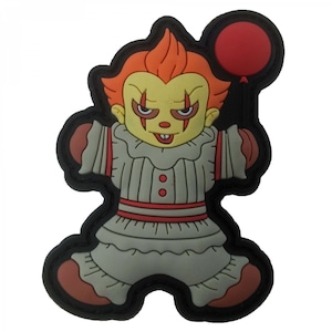 May include: A cartoon-style patch featuring a clown with orange hair, yellow skin, and a gray outfit with red accents. The clown is holding a red balloon. The patch has a black border and a brown outline.