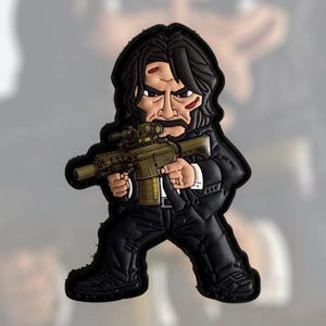 Może przedstawiać: Naszywka w stylu kreskówki przedstawiająca postać w czarnym garniturze, trzymającą karabin z lunetą. Postać ma długie czarne włosy, wąsy i obrażenia twarzy. Naszywka jest głównie czarna, z brązowymi i oliwkowymi akcentami na karabinie.