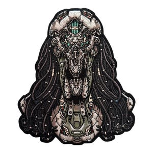 May include: A black and gray embroidered patch of a creature with a mechanical head and long black hair. The creature has a green and gray face with a large mouth and sharp teeth.