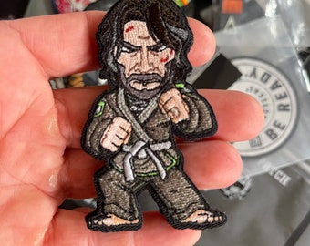 May include: Embroidered patch featuring a cartoon character in a black gi with a white belt, green accents, and a black beard. The character has a serious expression and is in a fighting stance.