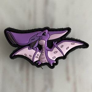 May include: Purple cartoon pterodactyl with a pink underbelly and black outline. The pterodactyl is flying with its wings spread out.
