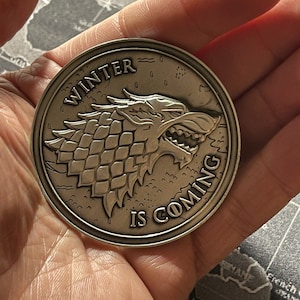 May include: A silver coin with a wolf head and the words "Winter is Coming" on it.