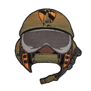 May include: Embroidered patch depicting a military pilot's helmet with a visor. The patch uses olive green, orange, and grey. The design includes the helmet's shape, visor, and a small emblem, suitable for application on clothing.