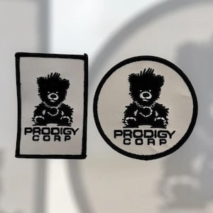 May include: Two patches: one rectangular, one circular. Both feature a black teddy bear design with a chain necklace and the text "PRODIGY CORP" in black. The patches have a white background and black borders.