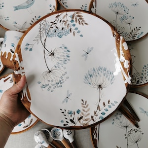 May include: A set of white ceramic plates with a brown rim and a delicate floral design featuring blue flowers, brown leaves, and dragonfly accents.