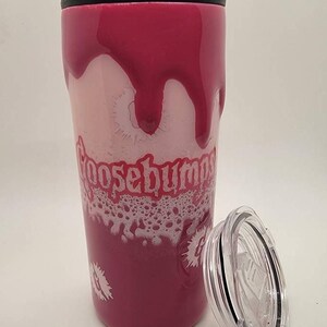 May include: A pink and white stainless steel tumbler with a black lid and a Goosebumps logo. The tumbler has a dripping effect with white foam around the logo.
