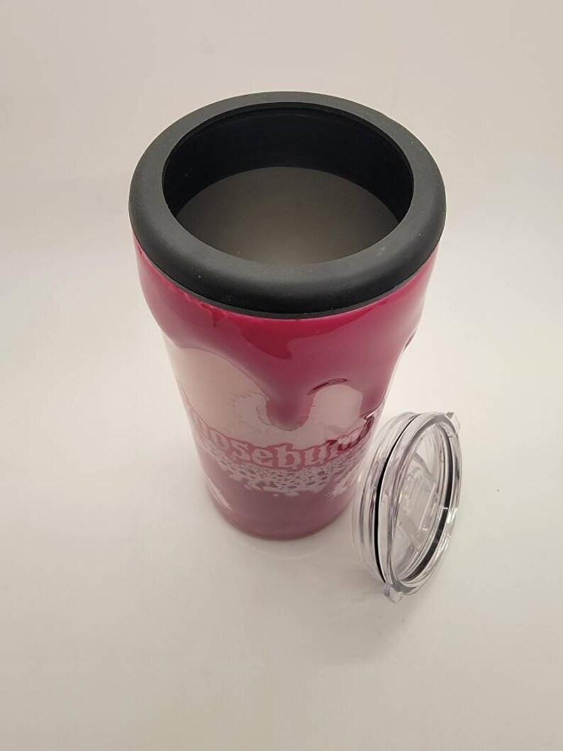 May include: A pink stainless steel tumbler with a black lid and a white design that says "Rosebud". The tumbler has a clear plastic lid with a black ring around the edge.