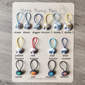May include: A set of 10 colorful hair ties with different fabric designs. The designs include construction vehicles, tractors, and planets. The hair ties are labeled with the names of the designs, such as "crane", "dozer", "digger", "tractor 1", "dump 1", "dump 2", "yellow tractor", "red tractor", "teal tractor", "blue tractor", "earth", "sun", "neptune", and "saturn". The text "Mama Bunny Bows" and the website address "www.mamabunnybows.com" are also included.