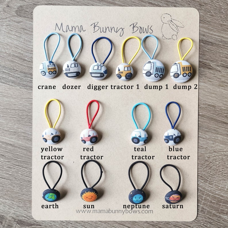 May include: A set of 10 colorful hair ties with different fabric designs. The designs include construction vehicles, tractors, and planets. The hair ties are labeled with the names of the designs, such as "crane", "dozer", "digger", "tractor 1", "dump 1", "dump 2", "yellow tractor", "red tractor", "teal tractor", "blue tractor", "earth", "sun", "neptune", and "saturn". The text "Mama Bunny Bows" and the website address "www.mamabunnybows.com" are also included.