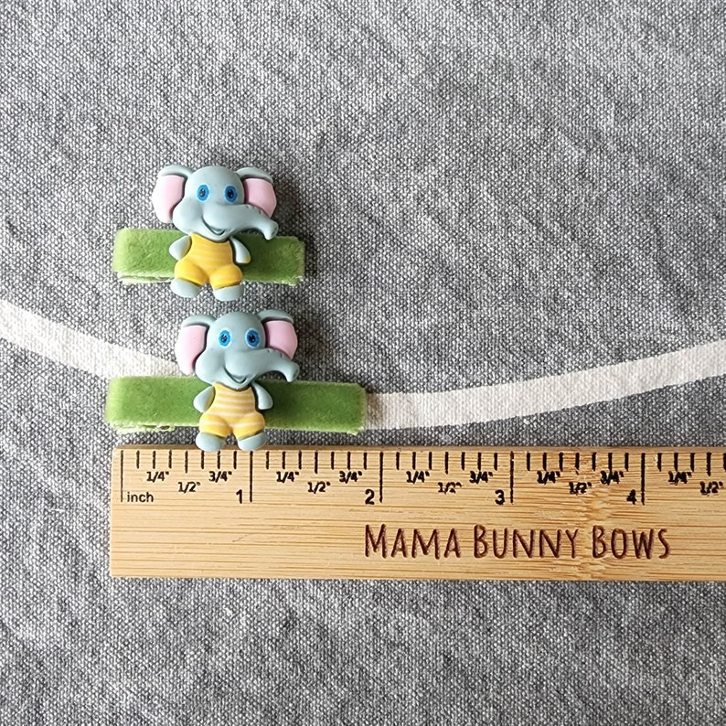 May include: Two green fabric hair ties with blue and yellow elephant charms. The hair ties are 5 cm long. The ruler reads "MAMA BUNNY BOWS".