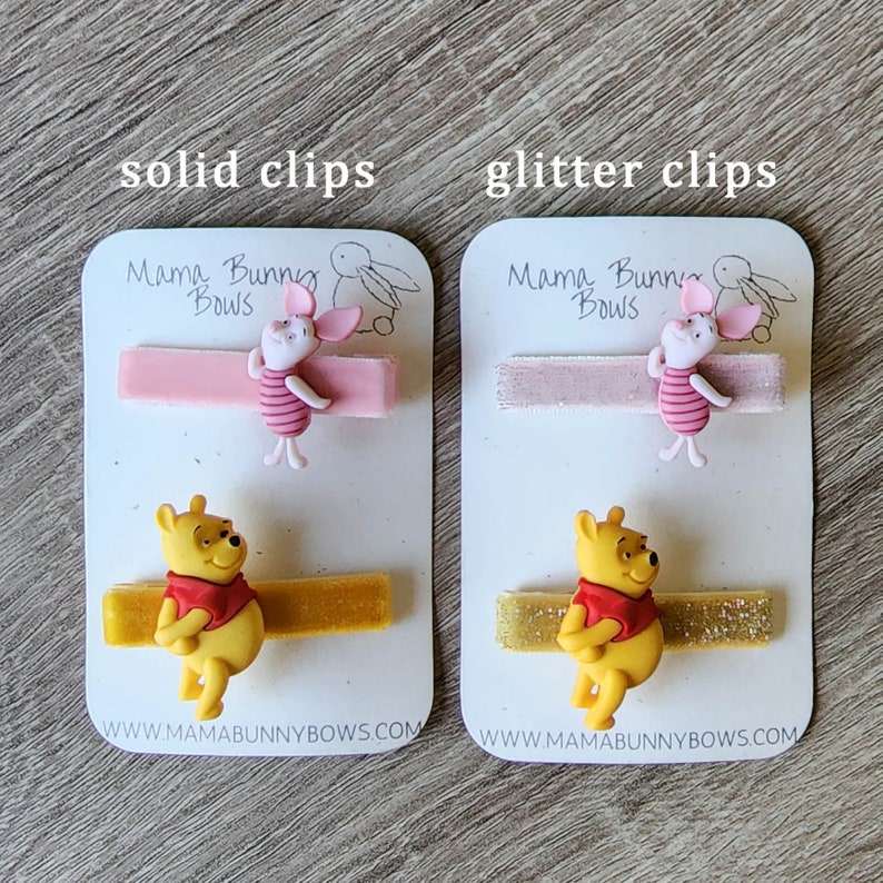Puede incluir: Dos juegos de pinzas para el pelo con los personajes de Winnie de Pooh y Piglet. El juego de la izquierda tiene pinzas rosas y amarillas s&oacute;lidas, mientras que el juego de la derecha tiene pinzas rosas y amarillas con purpurina. Ambos juegos tienen el texto "Mama Bunny Bows" y una direcci&oacute;n de sitio web.