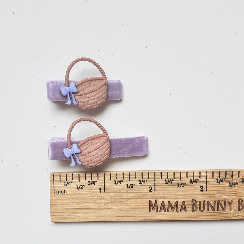 Puede incluir: Dos pinzas para el pelo de terciopelo morado con abalorios de cesta de mimbre marr&oacute;n y lazos de color morado claro. Las pinzas se muestran junto a una regla de madera con marcas en pulgadas.