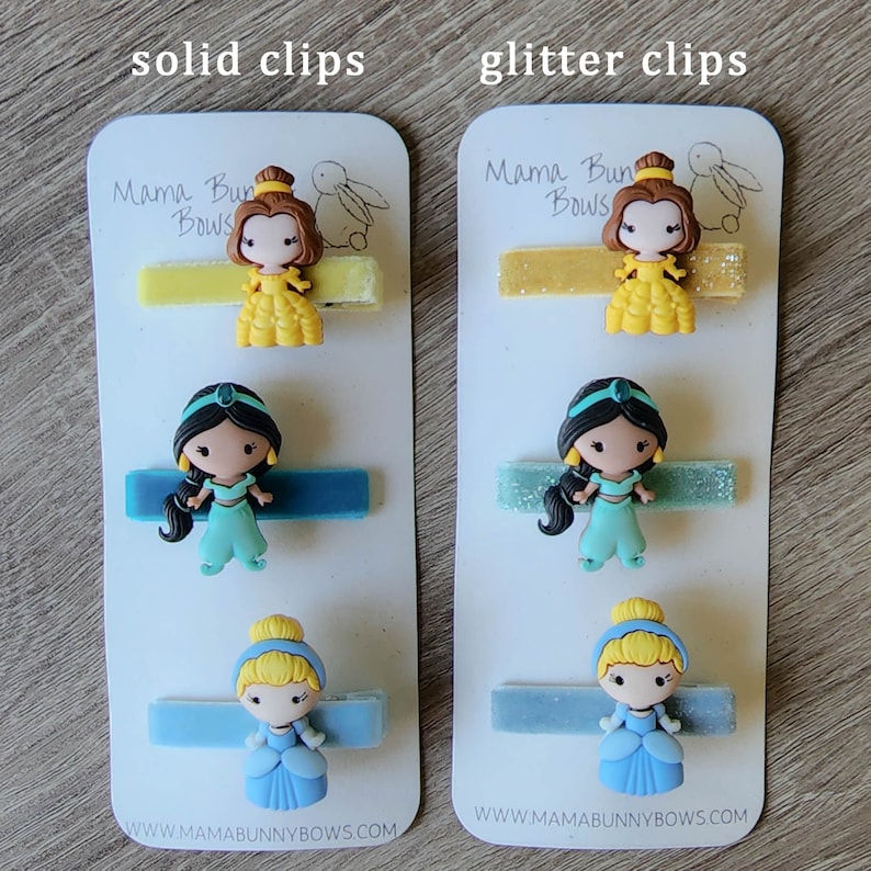 May include: Two sets of hair clips featuring Disney Princess characters. The set on the left has solid colored clips, while the set on the right has glitter clips. Both sets include Belle, Jasmine, and Cinderella.