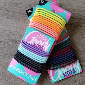 May include: Two packages of Goody Kids ouchless hair elastics. Each package contains 30 hair ties in a variety of colors. The text on the package reads "Goody Kids Ouchless Damage-Free Hold Attache Sans Abimer #1 in Ouchless Styles Elastics/&Eacute;lastiques".