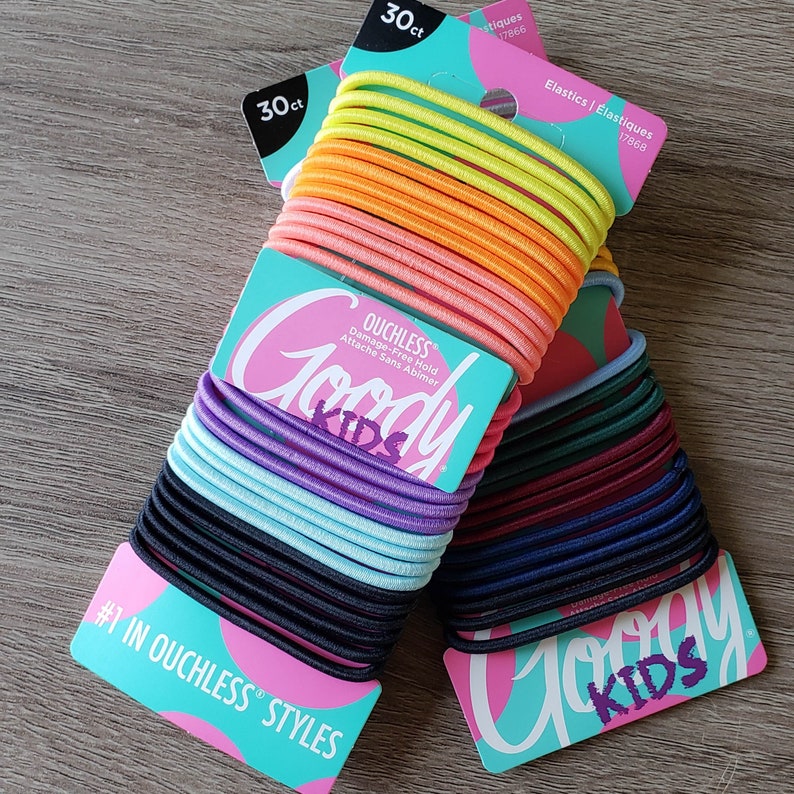May include: Two packages of Goody Kids ouchless hair elastics. Each package contains 30 hair ties in a variety of colors. The text on the package reads "Goody Kids Ouchless Damage-Free Hold Attache Sans Abimer #1 in Ouchless Styles Elastics/&Eacute;lastiques".