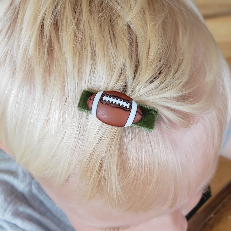 May include: A green velvet hair clip with a brown and white football design.