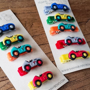 May include: A set of 10 colorful car-shaped hair clips with velvet ribbon accents. The clips feature a variety of colors, including red, yellow, blue, green, and gray. The clips are perfect for adding a touch of whimsy to any hairstyle.