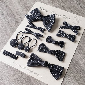 May include: A set of black and white hair bows with a heart pattern. The bows are arranged on a brown card with the text "Mama Bunny Bows" and a website address.