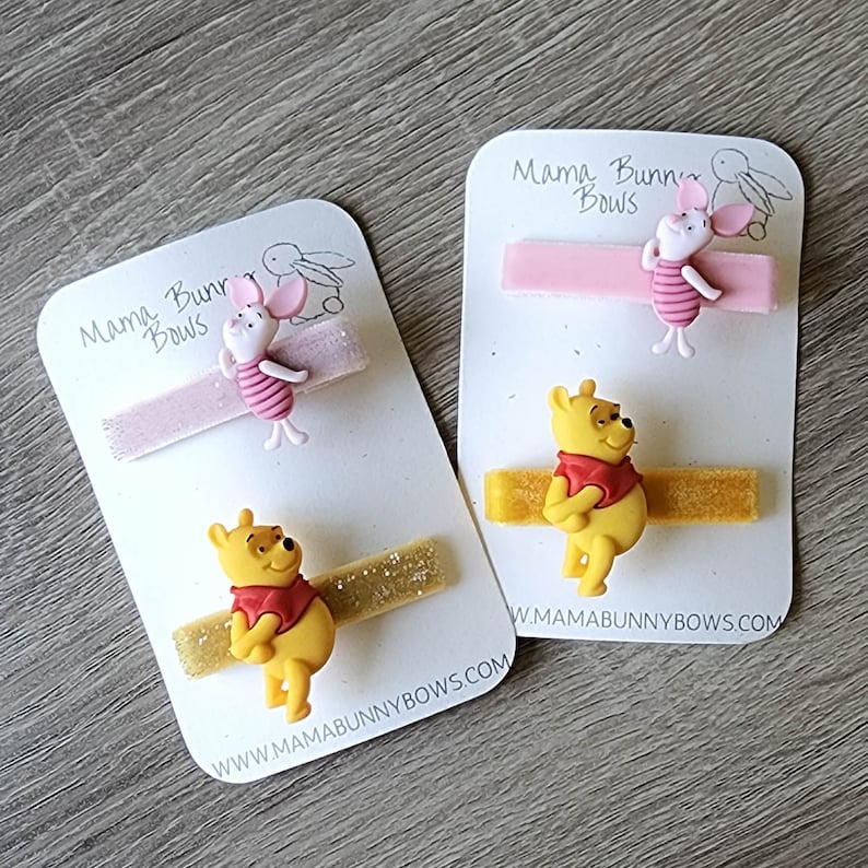Puede incluir: Dos juegos de pinzas para el pelo con los personajes de Winnie de Pooh y Piglet. Cada juego incluye una cinta de brillo rosa o amarilla con un amuleto de personaje a juego. Las tarjetas tienen el texto "Mama Bunny Bows" y una direcci&oacute;n de sitio web.