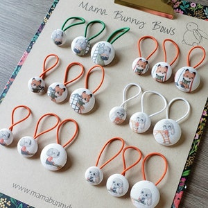 May include: A set of 10 hair ties with colourful fabric buttons featuring various animal designs. The buttons have images of foxes, bunnies, and other woodland creatures. The hair ties are available in orange and white.