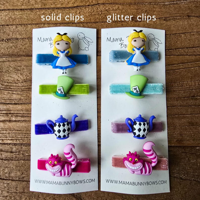 Op de afbeelding: Twee sets haarclips met personages uit Alice in Wonderland. Elke clip heeft een ander personage: Alice, de hoed van de Mad Hatter, een theepot en de Cheshire Cat. De tekst "solid clips" en "glitter clips" staat bovenaan.