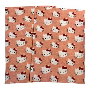 May include: Three pink fabric squares with a repeating pattern of white cartoon cats with red bows.
