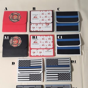 May include: A collection of small, square, hinged wallets with various designs. Some feature the American flag with a blue stripe, others have firefighter emblems or patterns with fire trucks and the text "AMERICAN FIRE FIGHTER".