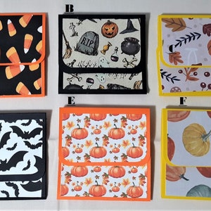 May include: A collection of six Halloween-themed small square gift boxes. The boxes feature various patterns, including candy corn, bats, pumpkins, and fall leaves. Each box has a contrasting border color.