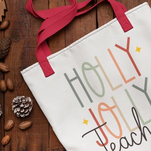 May include: White canvas tote bag with red handles. The bag has a colorful design that says "Holly Jolly Teacher" with a star accent.