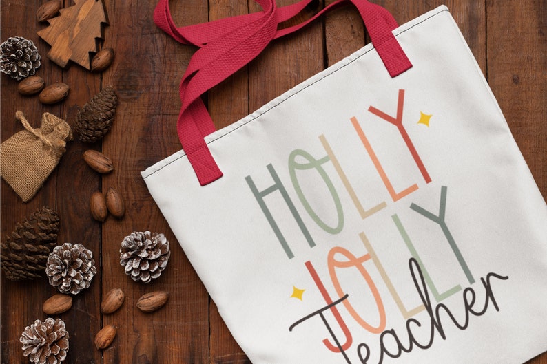 May include: White canvas tote bag with red handles. The bag has a colorful design that says "Holly Jolly Teacher" with a star accent.
