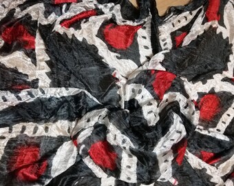 Puede incluir: Una tela con estampado en blanco y negro con acentos rojos. La tela está arrugada y tiene una textura suave y fluida.
