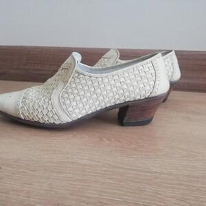 May include: Off-white woven leather shoes with a pointed toe and a low, stacked heel. The shoes have a slip-on design with a woven pattern across the upper. The heel is approximately 2 inches high.