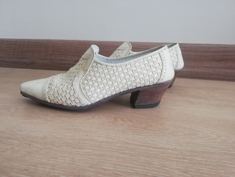 May include: Off-white woven leather shoes with a pointed toe and a low, stacked heel. The shoes have a slip-on design with a woven pattern across the upper. The heel is approximately 2 inches high.