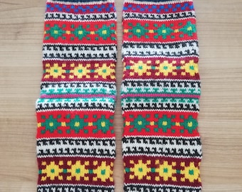 May include: A pair of knitted leg warmers with a vibrant, geometric pattern. The design features bands of red, white, black, and yellow, with green and blue accents. The cuffs are a deep navy blue, and the foot area is burgundy.