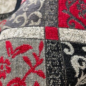 May include: Close-up of a multi-colored fabric with a patchwork design. The fabric is made of different textures and patterns, including a floral design, a geometric design, and a solid color. The fabric is red, black, white, and gray.