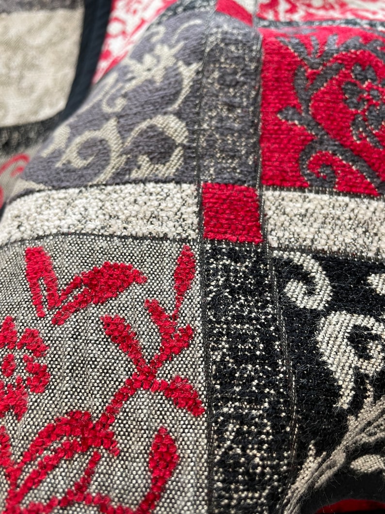 May include: Close-up of a multi-colored fabric with a patchwork design. The fabric is made of different textures and patterns, including a floral design, a geometric design, and a solid color. The fabric is red, black, white, and gray.