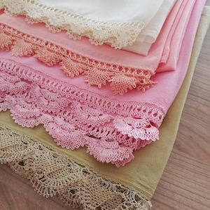 May include: A stack of four fabric squares with lace trim. The top square is white, the second is pink, the third is a darker pink, and the bottom square is a light green.