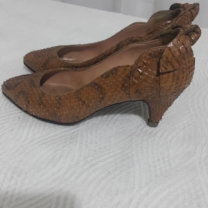 Op de afbeelding: Een paar bruine pumps met spitse neus en een textuur van slangenleer. De hakken zijn een lage, kitten heel stijl. De schoenen staan tegen een witte achtergrond.