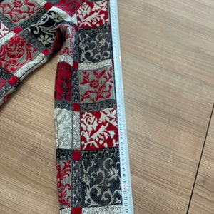 May include: A red, black, and white patterned jacket with a zipper closure. The sleeve is measured with a tape measure, showing a length of 58 cm.